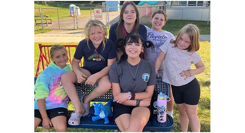 four smiling kids with their counselors sitting on a bench at the playground